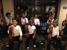 two rows of young students of color holding their classical guitars upright