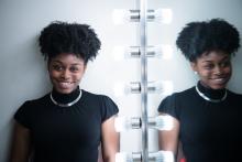 a young African American woman with an updo and a black top stands next to a dressing room mirror so her image is doubled