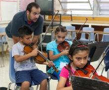 A teaching artist works with three students learning the violin.