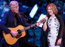 An older man playing a guitar next to a woman singing