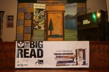 Many colorful posters, a podium, a piano, and a big NEA Big Read banner decorated on a stage.