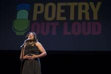 A teenage girl in a black dress speaks at a microphone with a Poetry Out Loud sign behind her.