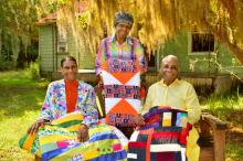 Three African-American women holding quilts