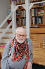 photo of children's book author and illustrator Tomie de  Paola at a wooden table with shelves of books in the background