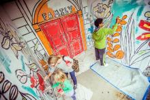 Three people work on filling in the colors on a wall mural 