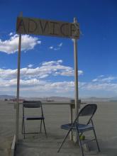 2 metal folding chairs under a banner that says "ADVICE' set amidst a desert landscape