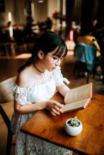 a young woman with glasses reads a book in a cafe
