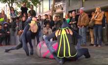 Dancers dressed as bugs dance on a city sidewalk for a crowd.