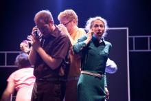 a man on a cell phone stands next to a woman who appears to be listening to something while another man stands behind them