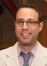 A headshot of a man with brown hair and glasses.