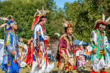 A group of four men in traditional regalia walking in a line outdoors.