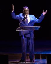 A man stands behind a podium with hands raised