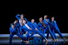 Six dancers dressed in blue on stage. 