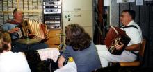 Two older white men seated in a radio station are playing accordions. 