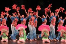Chinese American girls dressed in blue and pink holding fans and dancing on stage. 