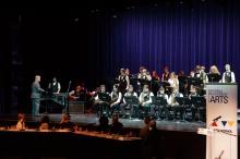 A student jazz orchestra is playing on stage while people seated at a table in front of the stage turn and watch. 