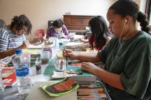 Group of kids sitting at table painting. 