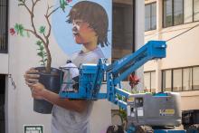 Man painting a mural of a child holding a potted plant