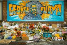 A painting of George Floyd on a building side with flowers in front of it. 