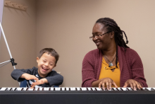 a young boy and an older woman sit at a piano keyboard