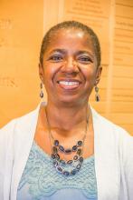 Photo of Akua Kouyate Tate wearing a blue top, white sweater, long earrings and a matching necklace with blue beads.