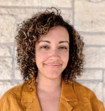 Photo of a woman with curly hair and a yellow shirt smiling