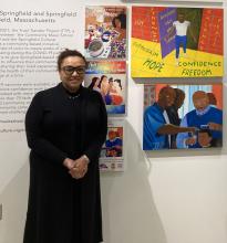 Woman in black dress wearing glasses standing in front of artwork at museum. 