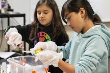 Two girls gluing items during an arts class. 