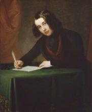 19th century portrait of a young Charles Dickens who sits over a desk covered with a green cloth writing