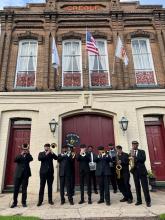 A band in uniforms plays in front of a two-story brick building.