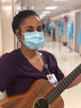 a woman of color in hospital scrubs and a hospital mask holding her guitar