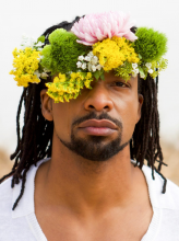 Headshot of a young man with a crown of flowers on his herad.
