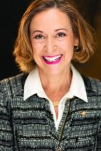 Portrait of a woman with short brown hair, smiling, wearing a blue striped sweater over a white shirt. 