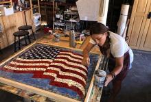 a woman working on a glass mosaic portrait of a rippling US flag