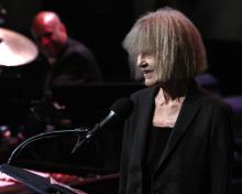Carla Bley stands behind a microphone