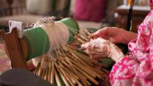 a close-up of an older woman's hands as she uses bobbins to make mundillo lace