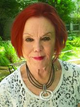 Portrait of an older woman with red hair wearing a lacy top outdoors. 