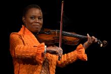Black woman in orange jacket playing a violin.