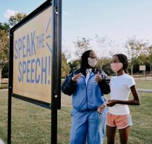An woman and a girl read a bill board in a park.