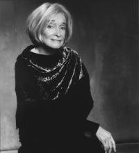 Older woman with blonde-gray hair wearing a black dress with scarf in portrait