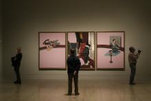 Masked museum visitors look at three large paintings by Francis Bacon