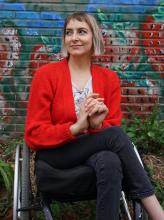 A woman in a wheelc hair osing in front of a colorful mural.