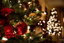 Christmas Tree with red ornaments and ribbon. There is a second lit Christmas tree in the back of the photo.