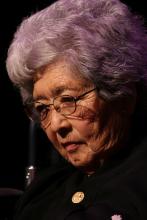 Japanese woman with gray hair and glasses looking down. 
