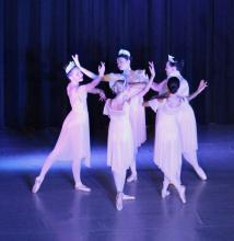 Five young ballerinas dance in a circle on stage.