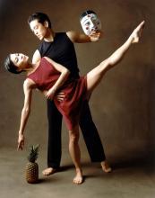 Woman in red dancing with man in black hold a mask.