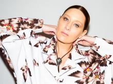 Photo of a Native woman wearing a white collared shirt that has Native print on it (designs with the following colors: brown, pink, orange, yellow, green, purple).