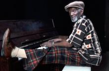 A man playing the piano with a leg up on the keybopard.
