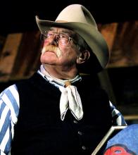 A man in a coboy hat sitting with a book on his lap.