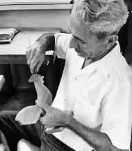 A man carving a wooden rooseter figurine.